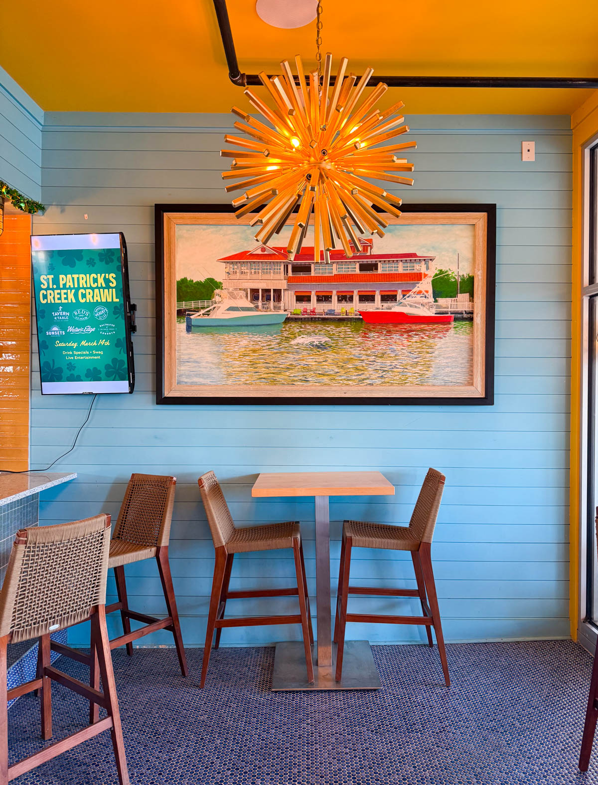 A table set against a blue wall with beachy art and a unique lighting fixture.