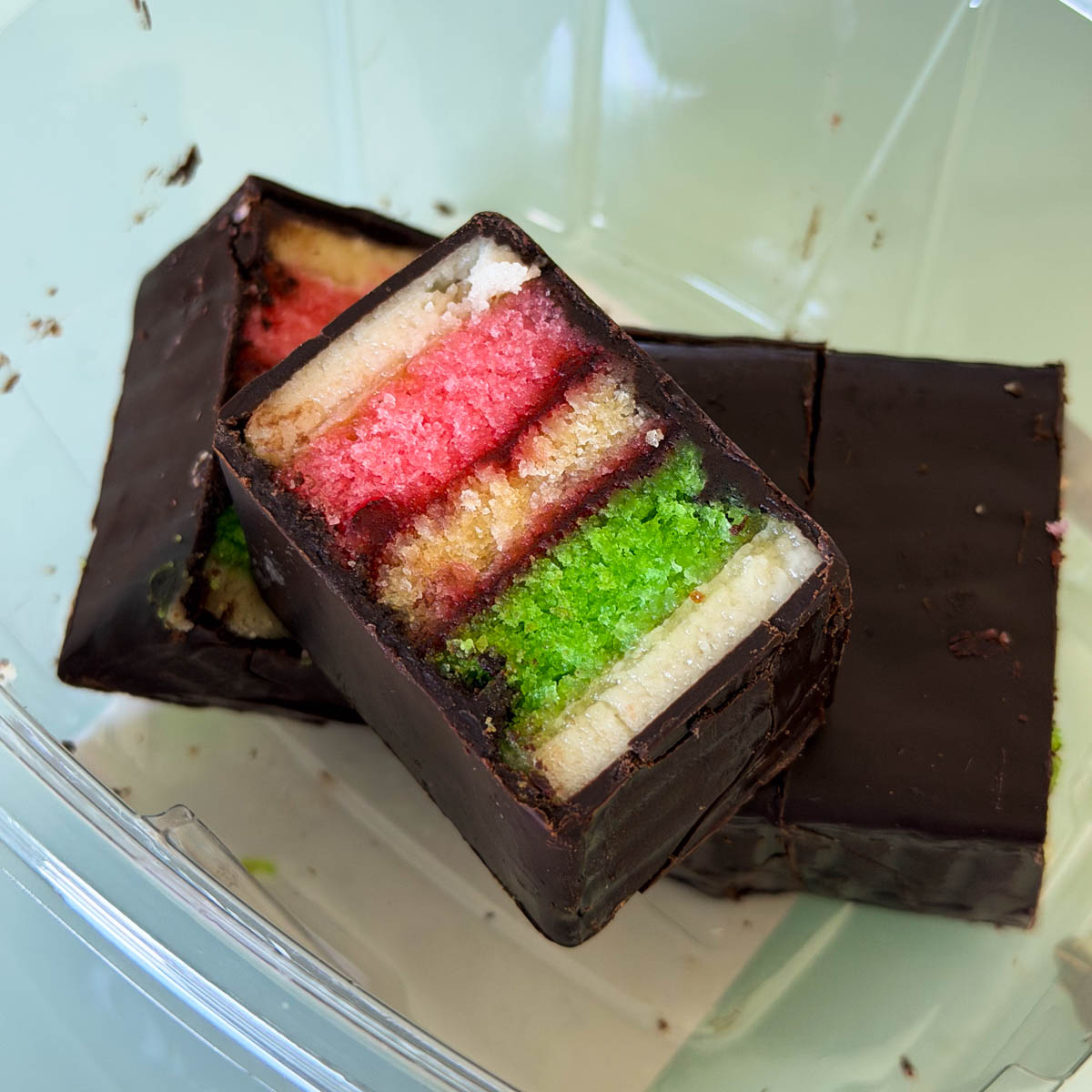A container of rainbow cookies (a chocolate covered cake-like cookie with pink and green layers)