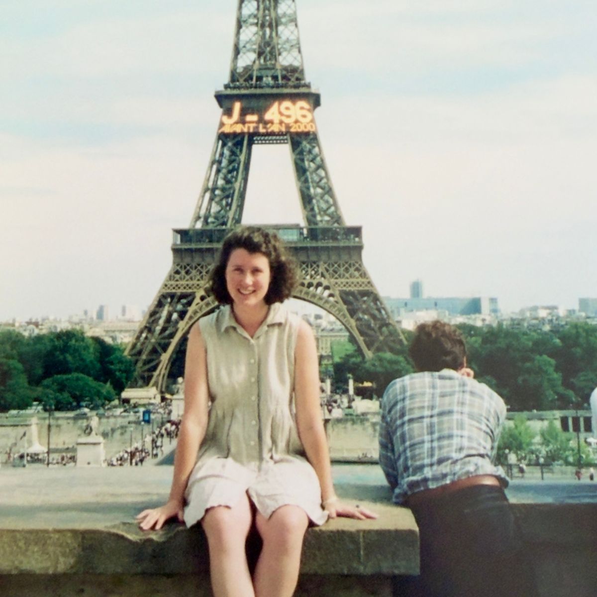 A vintage photo of a young woman sitting in front of the Eiffel Tower which is lit up with the numbers counting down to New Year's Eve 2000.