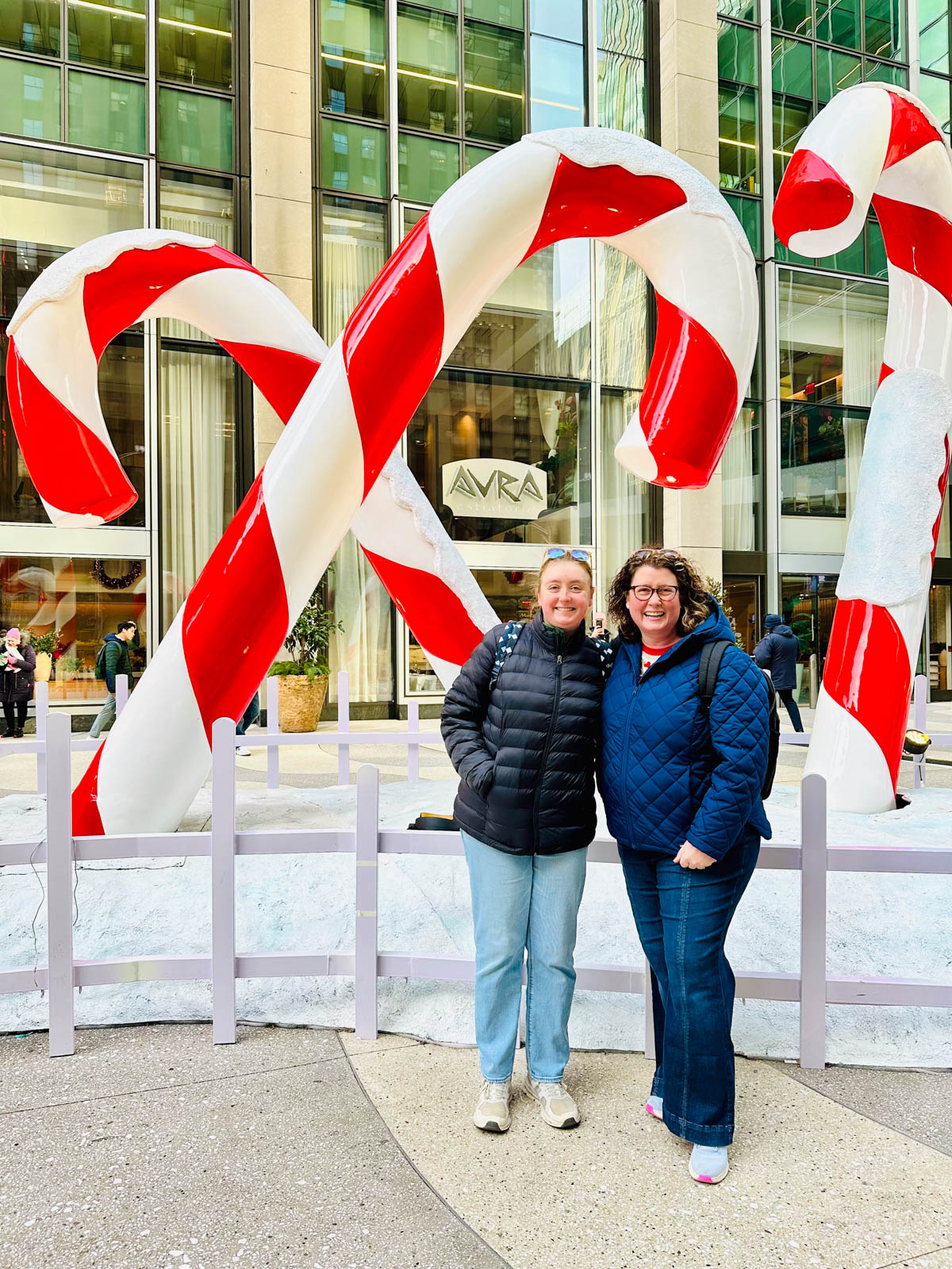 A mom and daughter stand in front of a giant candy cane art installation on Fifth Avenue in New York. 